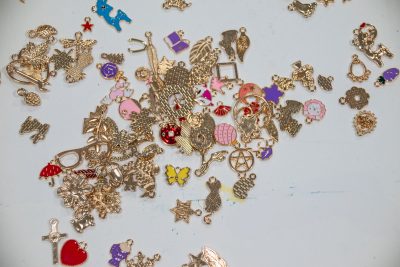 A collection of various small, colorful metal charms scattered on a white surface. The charms are in different shapes, including animals, stars, butterflies, and hearts, with some painted in bright colors like red, purple, and gold.