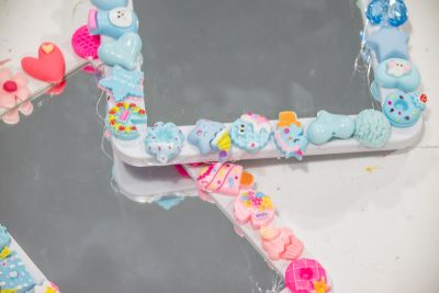 Three mirrors with white frames decorated with colorful polymer clay charms, including hearts, stars, animals, and sweets in pastel colors such as pink, blue, and yellow, are placed on a white surface.