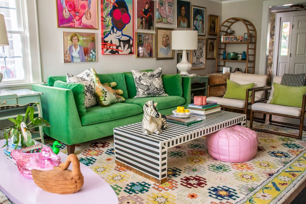 A living room with a green sofa, two armchairs, and a black-and-white striped coffee table topped with a zebra figurine, sitting on a colorful patterned rug in front of a gallery wall.