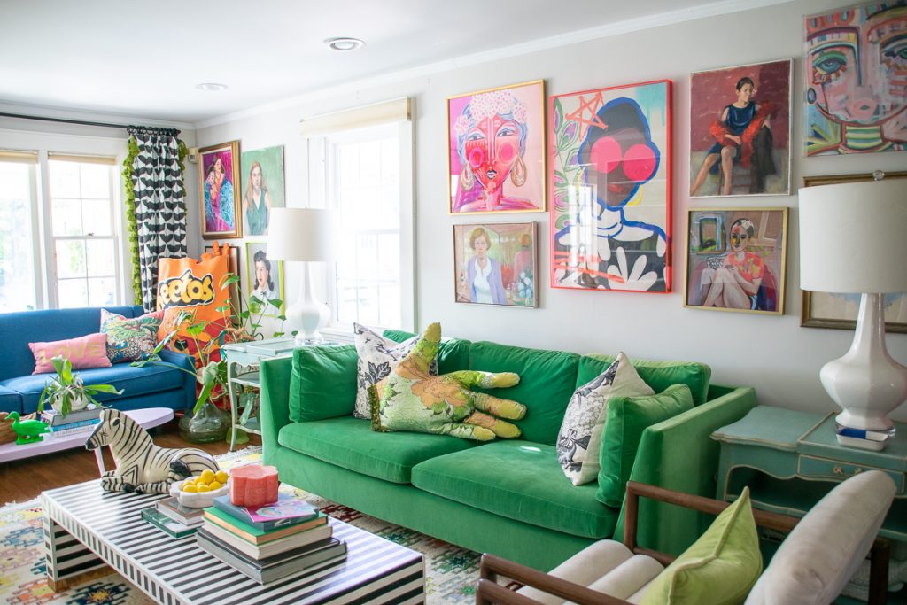 A living room with a green sofa, a striped coffee table, and walls decorated with numerous colorful portraits.