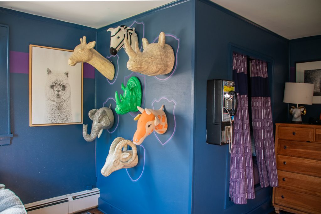 Six stylized animal head wall mounts arranged on a blue wall next to a vintage wall-mounted payphone.
